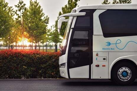 Side view of a coach on the road. Foliage and trees in the background with the sun setting.